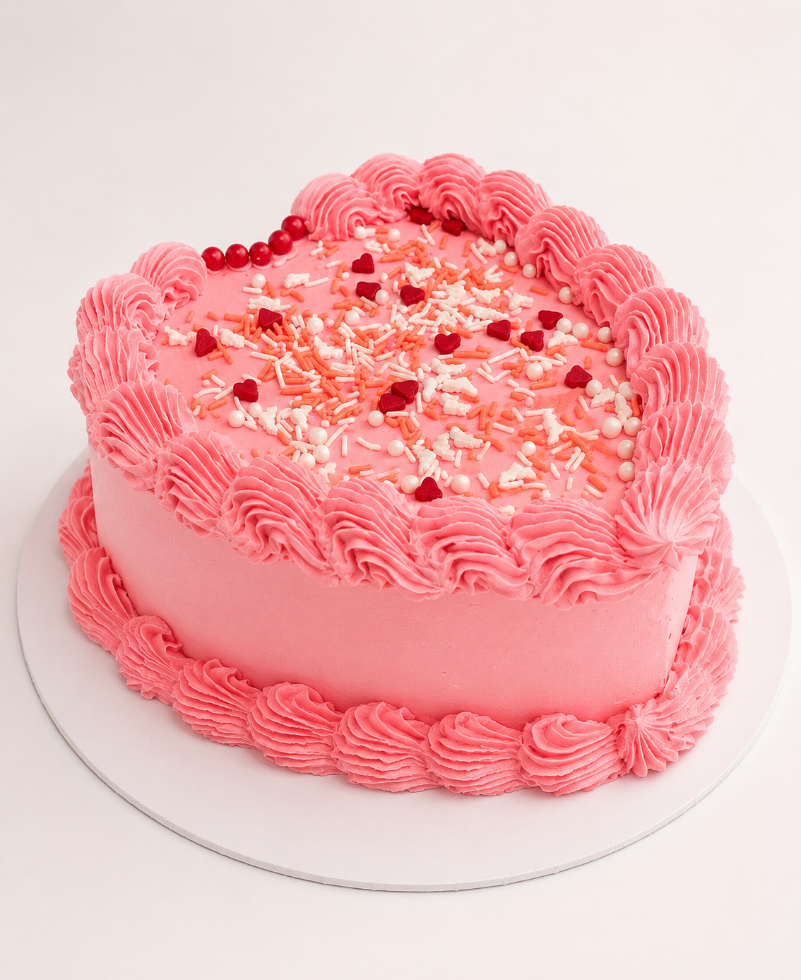 Pink heart-shaped cake with sprinkles and piped buttercream border